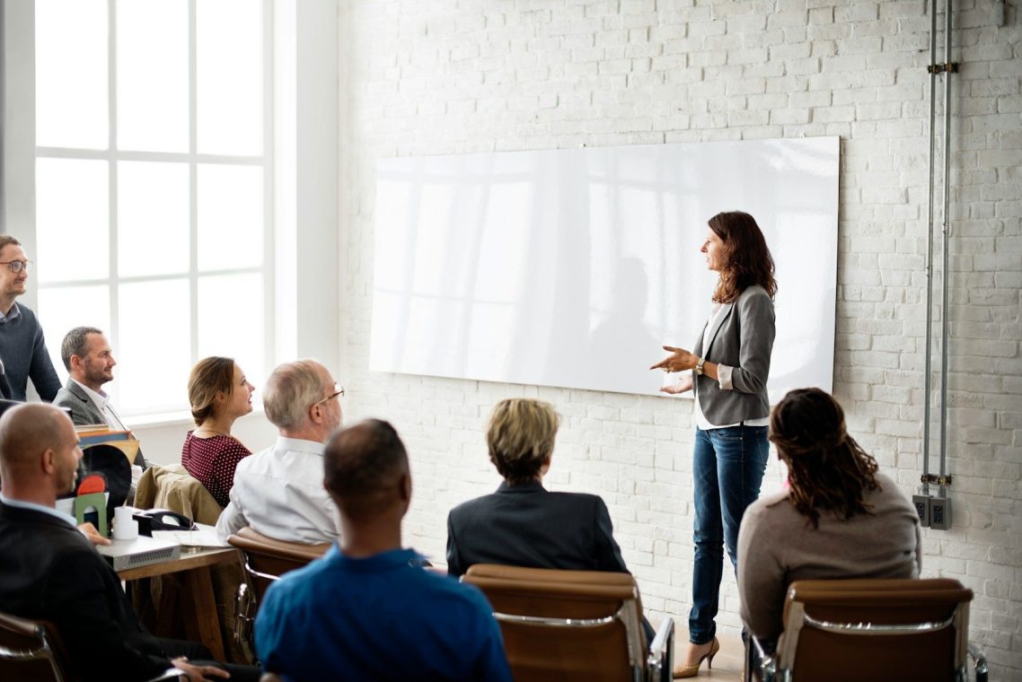 Bold Leadership Path Solution Page A woman presents to an audience in a modern conference room.